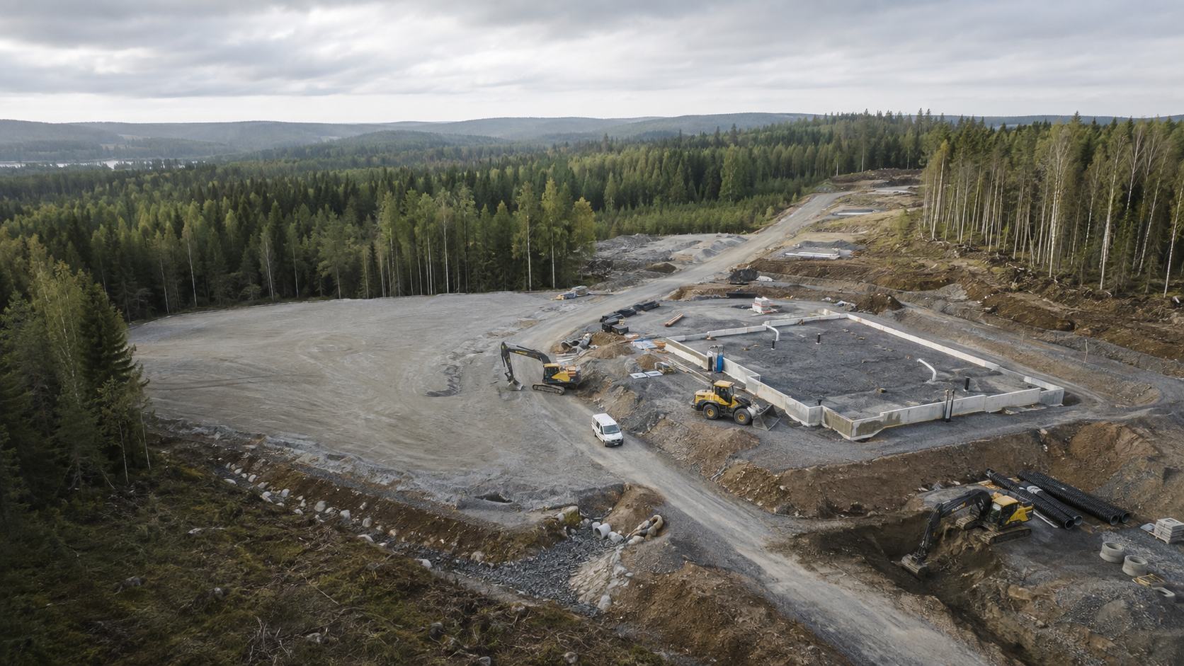 Ilmakuva rakennustyömaasta metsän keskellä: perustukset, kaivinkoneet ja pyöräkuormaaja.